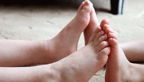 Two pairs of bare feet resting together on a carpet
