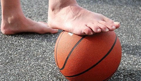 Bare foot resting on a basketball on pavement